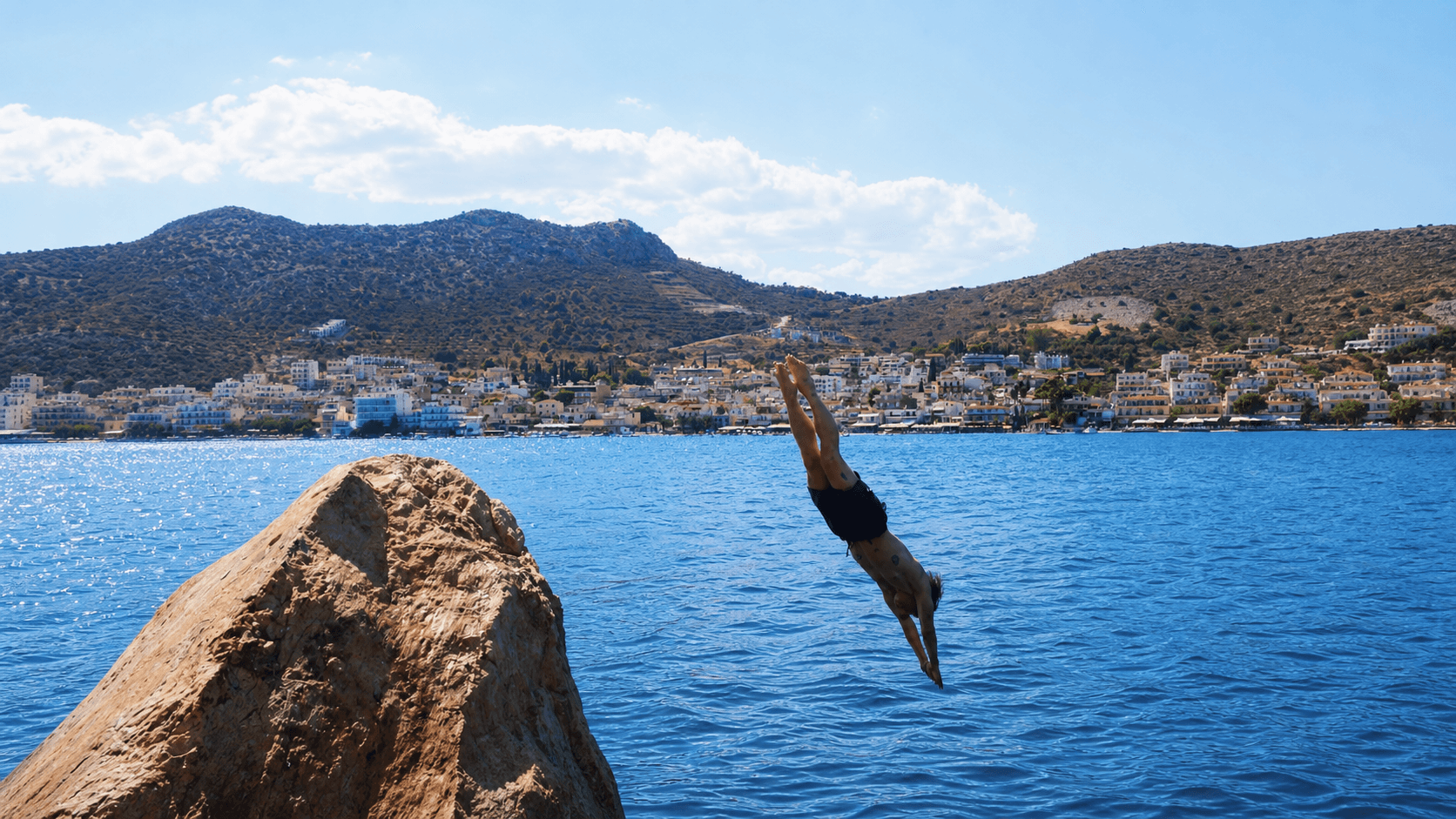 Swimmer jumping from a seaside cliff into clear water